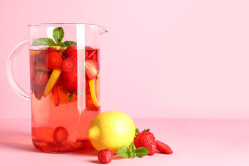 Jug of infused water with strawberry and lemon on pink background