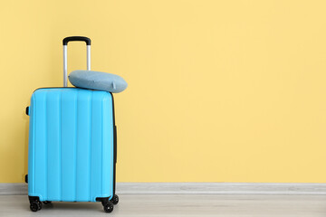 Obraz premium Blue suitcase with travel cushion near yellow wall. Travel concept