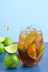 Glass of cold Cuba Libre cocktail and limes on blue table