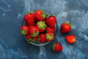 Glass bowl with fresh strawberries on blue background