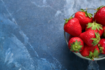 Glass bowl with fresh strawberries on blue background