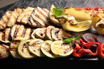 Wooden board with tasty grilled vegetables on black background