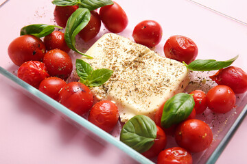 Baking dish with tasty tomatoes and feta cheese on pink background