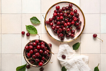 Bowl and plate with sweet cherries on light tile background