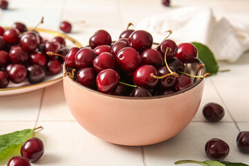 Bowl and plate with sweet cherries on light tile background