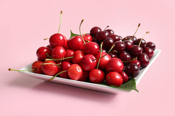 Plate with sweet cherries on pink background