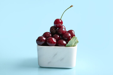 Bowl with sweet cherries and leaf on blue background