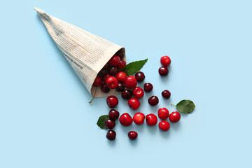 Newspaper with sweet cherries on blue background