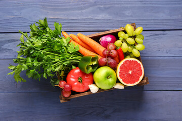 Box with different fresh fruits and vegetables on blue wooden background