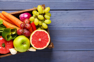 Box with different fresh fruits and vegetables on blue wooden background, closeup