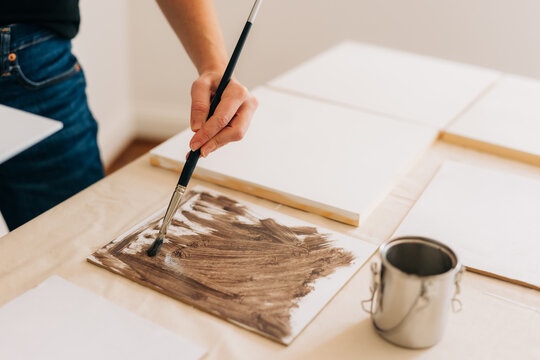 An artist is painting one canvas brown while she has a blank canvas next to her hand. 