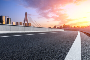 Fototapeta premium Asphalt road and urban skyline with modern buildings at sunrise