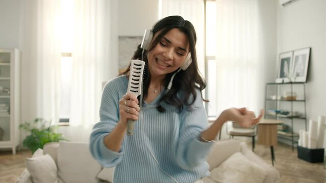 Joyful people lifestyle concept, dancing singing in hair brush in modern apartment on motion background. Portrait of crazy carefree latin american girl having fun. Funny hispanic woman dancing hands