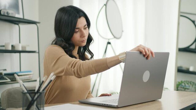 Focused latin female working remotely in modern living room. Side view dolly shot of confident hispanic brunette woman open and typing on modern laptop. Professional girl writing email in home office