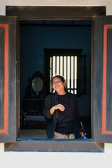 Woman standing behind an old black wooden window of an old Chinese house