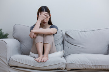 Female having depression sitting alone in bedroom corner. woman headache unhappy emotion. Sitting alone on sofa. Anxiety despairing mental health problems.