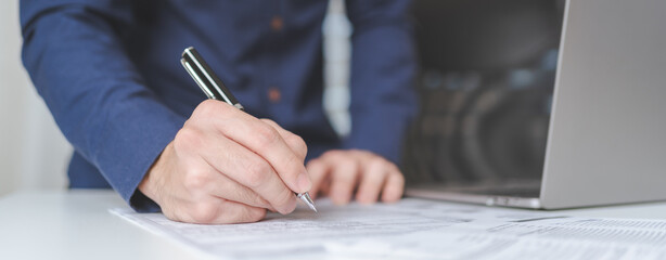 Businessman hand holds pen, writing on business paperwork for accept agreement contract on business investment project. Young adult business man signing on financial document deal. Copy space. Banner. - 617247347
