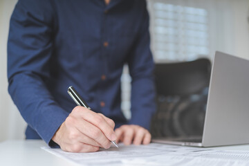 Businessman hand holds pen for writing on business paperwork for accept agreement contract on business investment or project. Young adult business man signing on financial document deal. Copy space - 617247352