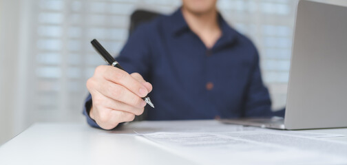 Hand of businessman holds pen for writing on business paperwork for accept agreement contract on business investment or project. Young adult business man signing on financial document deal. Banner. - 617247362
