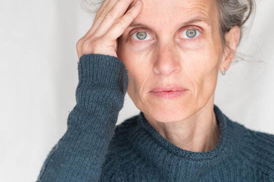 Close up portrait of older woman in blue sweater with hand on head looking at camera (selective focus)