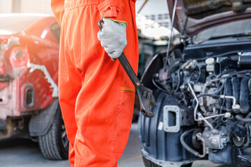 Side view of a male mechanic in orange clothes Craftsman holding a large wrench working in a car...