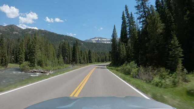 POV Driving a car on asphalt road along the river in Yellowstone National Park. Blue sky on sunny day