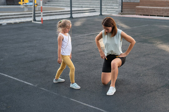 Mother and daughter go in for sports outdoors. Caucasian woman and little girl are engaged in fitness at the stadium.