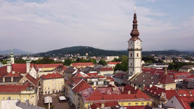 Clock tower of Klagenfurt chapel standing out above red roofs, aerial pullback