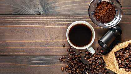 Coffee background, top view with copy space. Black cup of coffee, ground coffee, mill, bowl of roasted coffee beans on dark wooden background