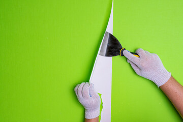 Men's gloved hands remove old wallpaper from the wall with a spatula. Background with hands doing...