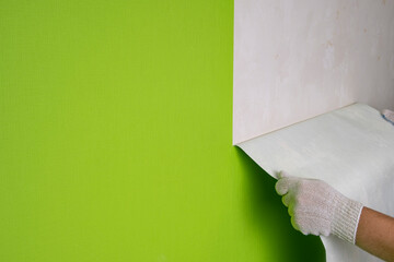 Gloved hands remove wallpaper from the wall in the room.