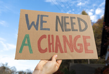 Woman holding placard sign with text We Need A Change. Female protestor with cardboard banner at...