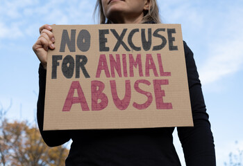 Woman holding placard sign with text No Excuse for Animal Abuse, during animals rights march. Protestor with cardboard banner at protest rally demonstration.