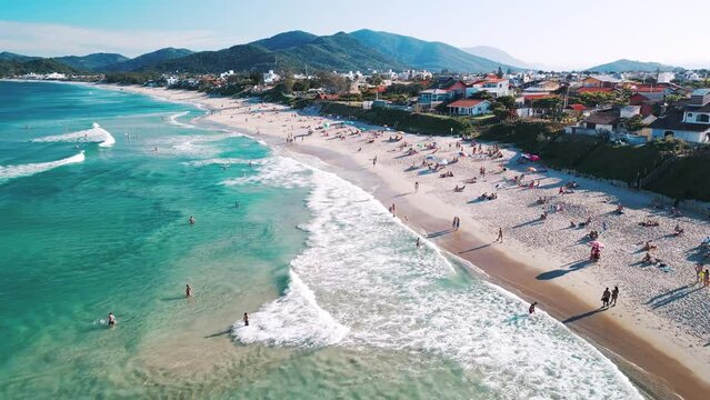 Aerial view of the sea with gentle waves and sandy beach with people relaxing on it. Lomba do Sabao beach on Santa Catarina island in Brazil