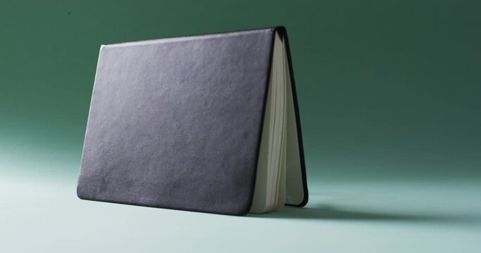 Close up of open black book standing horizontal with copy space on green background in slow motion