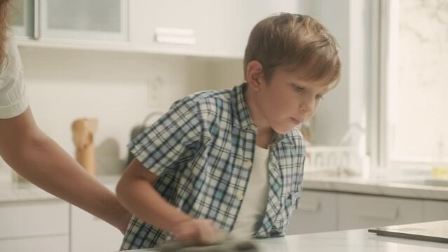 Mother and son doing housework together wiping table with detergent at kitchen