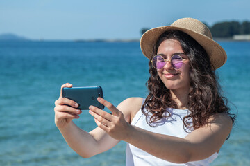 relaxed young woman taking a selfie or direct video with phone on the beach