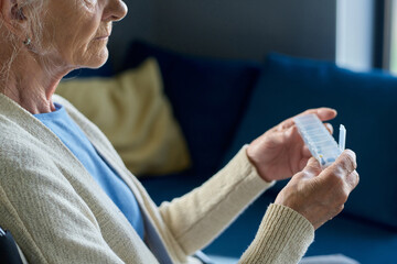 Close-up of female pensioner in casualwear holding small plastic pill-box with group of pills for therapy course while going to take one