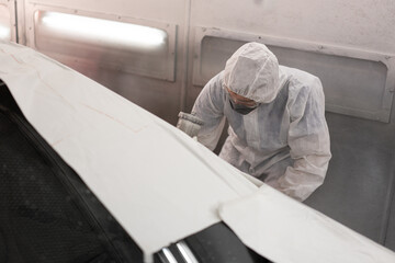 Worker painting a car in a special garage, wearing a white costume at car service	