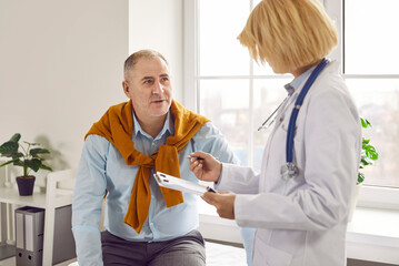 Mature man patient in medical clinic talking with female adult friendly doctor wearing stethoscope...