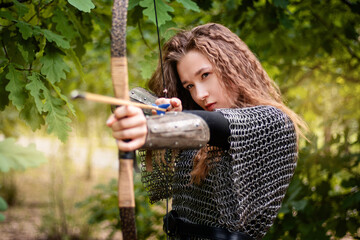 Medieval warrior woman in chain mail and bracers with a bow in her hands against the backdrop of an...