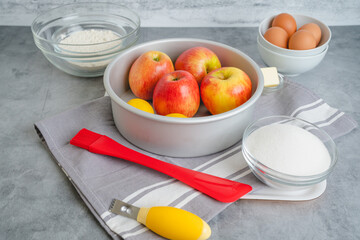 Baking pan, apples, lemons, eggs, sugar, and flour in bowls close-up on a kitchen table. Apple cake recipe
