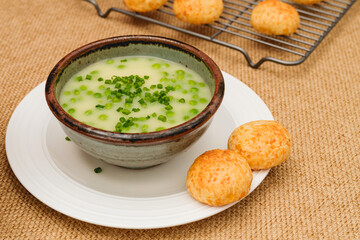 Celery cream soup with a green pea in a bowl garnished with chopped green onion and served with freshly baked cheese bread close-up