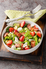 Delicious light salad of strawberries, avocado, bacon, lettuce, feta cheese close-up in a bowl on the table. Vertical