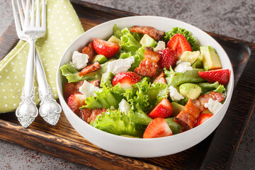 Salad with fresh strawberries, avocado, feta, bacon and lettuce on a wooden board close-up on the table. Horizontal
