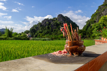 incense sticks on a fence overlooking a rice paddy with a mountain in the background in rural China