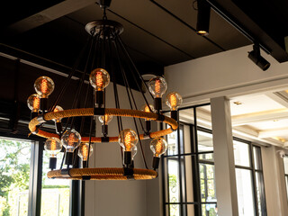 Fototapeta premium Modern chandelier in living room near glass window, loft style, vintage ceiling light or light bulbs hanging with from wooden ceiling, indoor, interior loft style building. Retro lighting decoration.