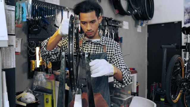Expert Asian young man fixing and spinning aluminum bike wheel with tools and equipment at bicycle repair shop. Asian craftsman wearing apron maintenance bike. Repair and Maintenance concept