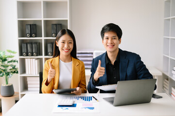 Obraz premium Two Asian business woman and man discuss investment project working and planning strategy with tablet laptop computer in office.