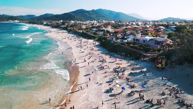 Aerial view of the sea with gentle waves and sandy beach with people relaxing on it. Lomba do Sabao beach on Santa Catarina island in Brazil